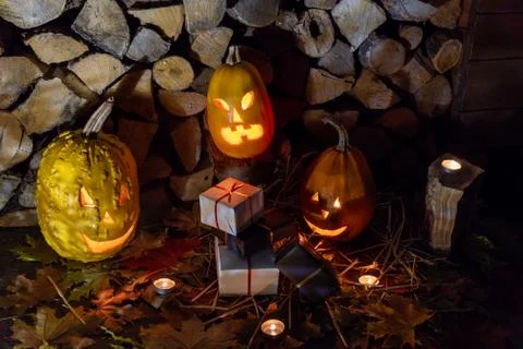 Three glowing pumpkins and a bunch of black and white gifts on fall foliage w Stock Photos