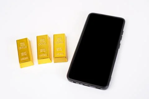 Three gold bars and a mobile phone with a black screen on a white background. Stock Photos