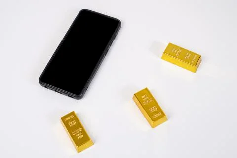 Three gold bars and a mobile phone with a black screen on a white background. Stock Photos