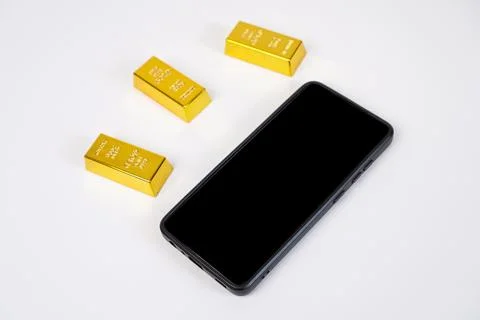 Three gold bars and a mobile phone with a black screen on a white background. Stock Photos