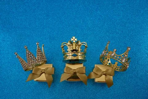 Three gold crowns on gift boxes on blue glittering background Foto stock