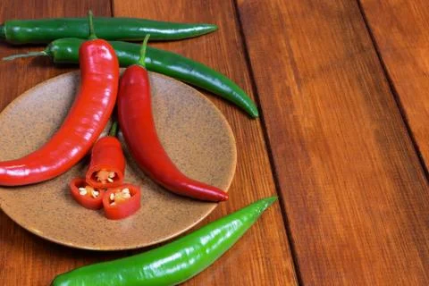 Three green and two red pods of chili pepper, as well as their slices, lie on Stock Photos