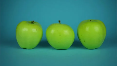 Three green apples rotating on blue background and going away. Stop motion 動画素材 245580476