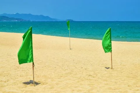 Three green flags on beach under sunlight near sea Stock Photos