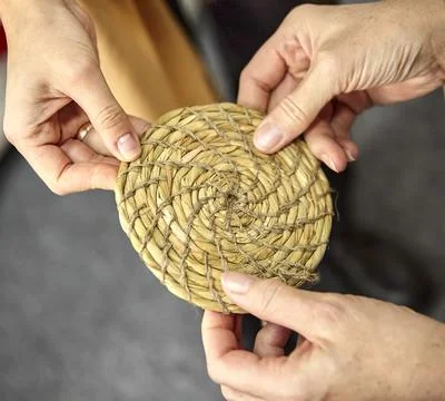 Three hands hold a round grass mat. Stock Photos