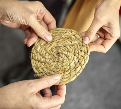 Three hands hold a round grass mat. Stock Photos