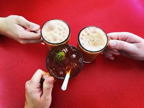 Three hands holding three beverages against a red background Stock Photos