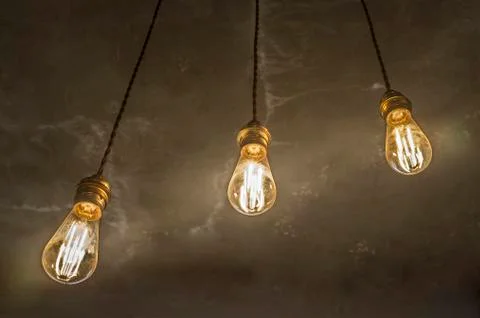 Three hanging light bulbs over oxide dark color concrete background Stock Photos