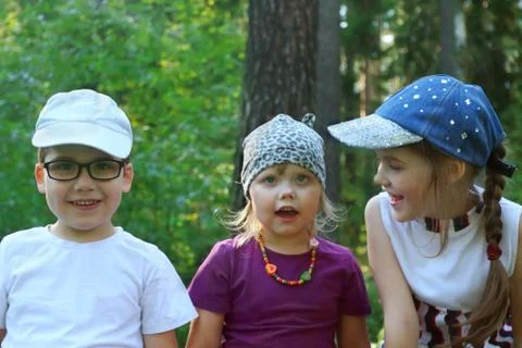 Three happy children sit, smile and talk in summer green sunny park Stock Photos