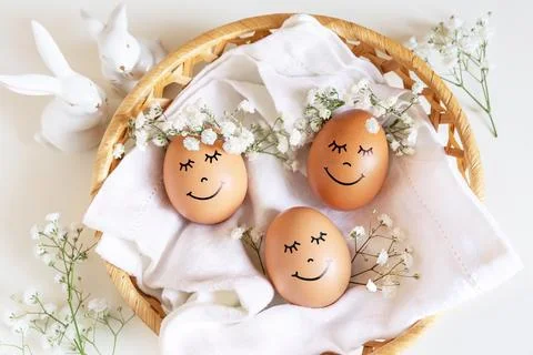 Three happy Easter eggs with cute faces in floral wreath crowns on white back Stock Photos