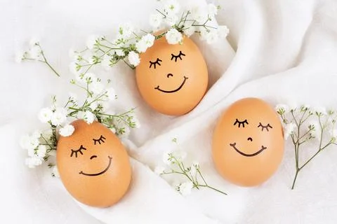 Three happy Easter eggs with cute faces in floral wreath crowns on white back Stock Photos