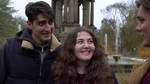 Three happy friends talking to each other near a fountain, laughing and smiling Stock-Footage 70818389