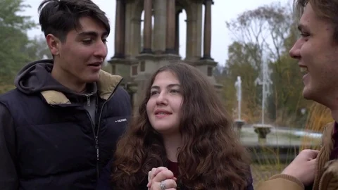 Three happy friends talking to each other near a fountain, laughing and smiling Video stock 70819089