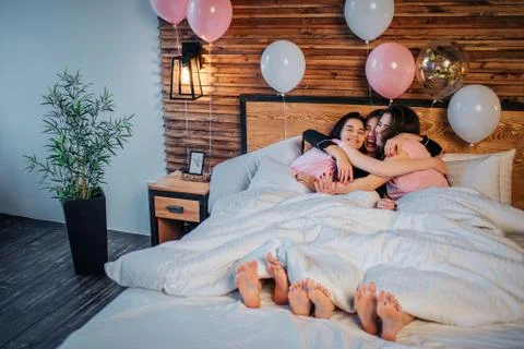 Three happy models lying under white blanket together and embracing. They smile Stock-Fotos