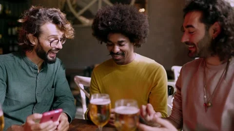Three happy multiracial friends using mobile phone sitting on table at bar. Stock Footage 281975326