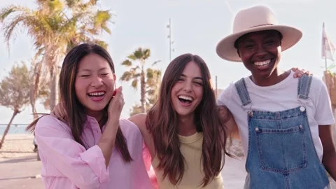 Three happy multiracial young beautiful girls enjoy day together hugging outdoor Stock Footage 250863001