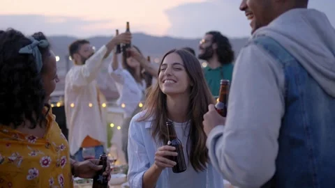 Three happy multiracial young people dancing at rooftop party with friends in Stock Footage 242881152
