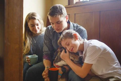 Three happy siblings cuddle their dog in beautiful golden window light Stock Photos