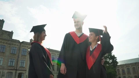 Three happy students in black and red mantles celebrating their graduation in Stock Footage 115652271