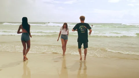Three happy, young, ethnically diverse, friends joke and play on the beach as th Stock Footage 199463724