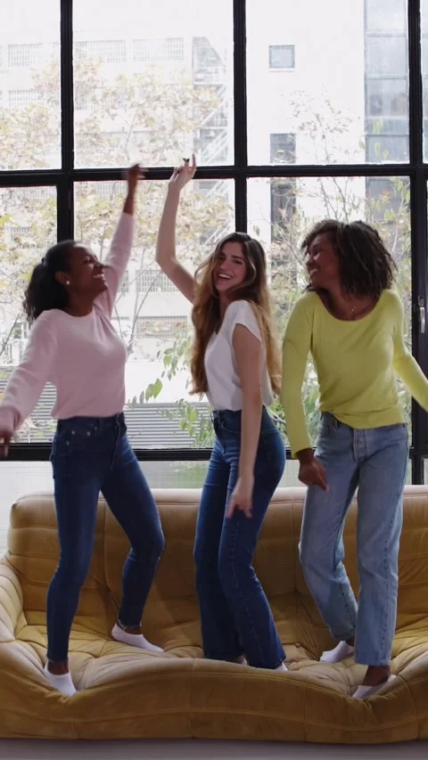Three happy young girls dancing on sofa at home Stock Footage 345386247