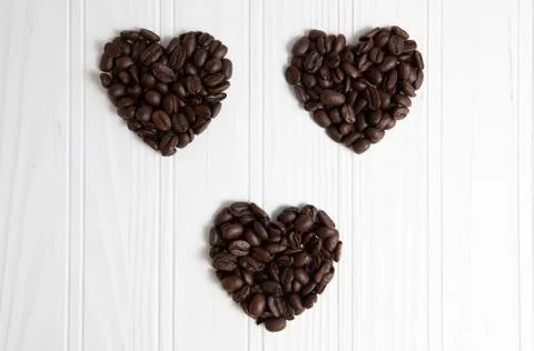 Three heart shape coffee beans in over a wood background Stock Photos