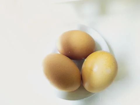 Three hen eggs on white small ceramic plate Stock Photos