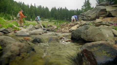 Three hikers cross a fresh water stream Stock Footage 59574729
