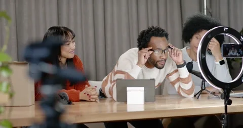Three hosts in studio ring light, right tapping phone, center testing eyeglasses Stock Footage 345590417