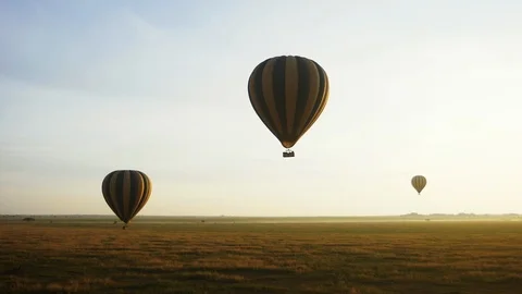 Three hot air balloons fly over a green valley in a cloudless sky Stock Footage 113733205