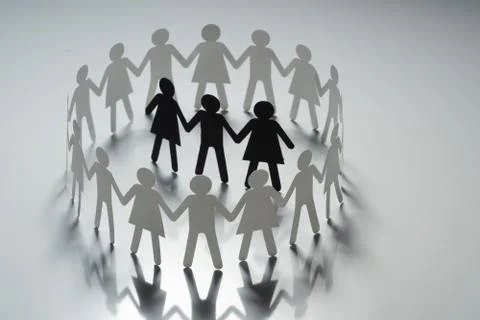Three human paper figures surrounded by circle of paper people holding hands on Stock Photos