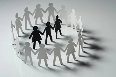 Three human paper figures surrounded by circle of paper people holding hands on Foto stock