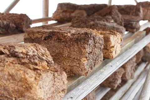 Three hunks of peat piled up for drying on wooden shelf with blurred backgrou Stock Photos