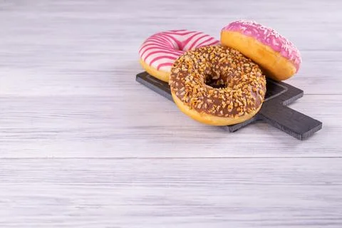 Three iced donuts are stacked on a pink black slate serving board Stock Photos