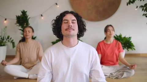 Three individuals are practicing meditation indoors in a calm space filled with  Stock Footage 346149227