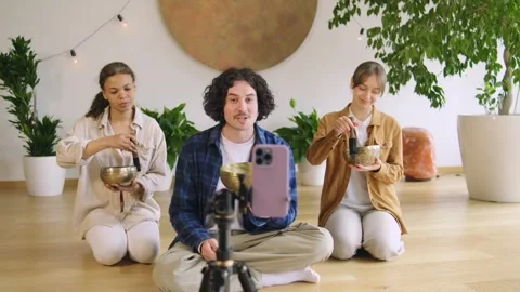 Three individuals are sitting on the floor in a studio, holding bowls and playin Stock Footage 346148693