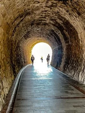 Three individuals traverse shadowed pathway, people moving towards glowing Stock Photos