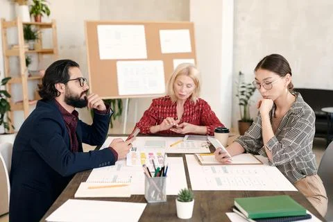 Three intercultural mobile application developers scrolling in smartphones Stock Photos