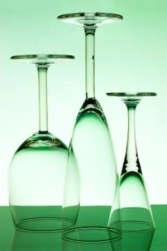 Three inverted empty glasses stand on a glass table on a green background Stock Photos