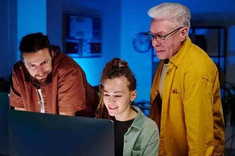 Three IT engineers looking at screen of desktop computer at night meeting Stock Photos
