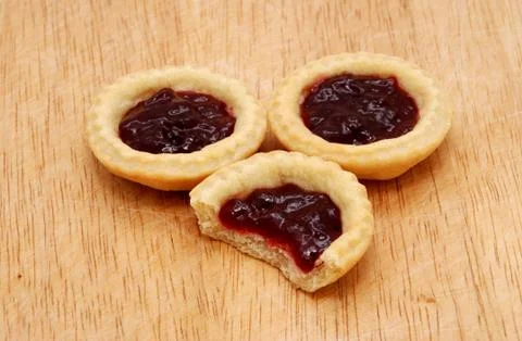 Three jam tarts, one with a bite taken, on a wooden table Stock Photos