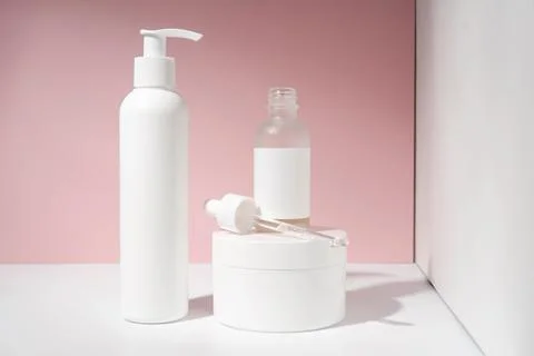 Three jars of cosmetics stand on a white and pink background. Stock Photos