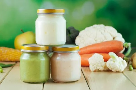 Three jars with vegetable puree on the light wooden background broccoli, caul Stock Photos