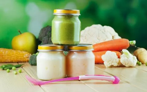 Three jars with vegetable puree on the light wooden background Stock Photos