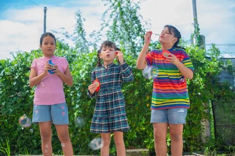 Three joyful children blowing bubbles in a sunny garden, surrounded by gree.. Stock Photos