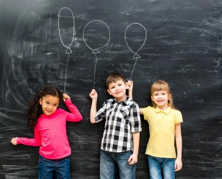 Three joyful children keep imaginary balloons drawn on the blackboard Foto stock