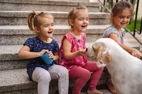 Three joyful sisters share laughter and treats with their pet dog Stock Photos