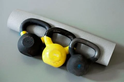 Three kettlebells and yoga mat on the grey background Stock Photos