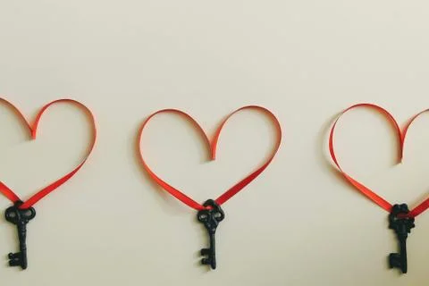 Three keys with a red ribbon in the shape of a heart on a light surface Stock Photos
