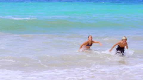 Three kids playing in the waves run out of the ocean and up the beach Stock Footage 33895632